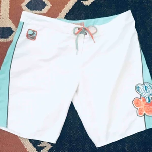  - Bad- eller surfshorts i snabbtorkande material. Öppning fram med kardborre. Hemlig ficka i linningen. Faux snörning fram