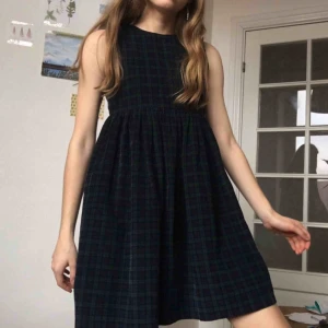  - En mörk rutig klänning som passar perfekt till både vinter och sommar. Manchesterliknande tyg. Mönster i svart, marinblå och mörkt grönt. Dragkedja där bak. Hög midja. Bara använd några få gånger. Går till lite över knäna på mig som är 1,67 :)