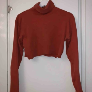  - En orange magtröja med långa ärmar och polokrage.