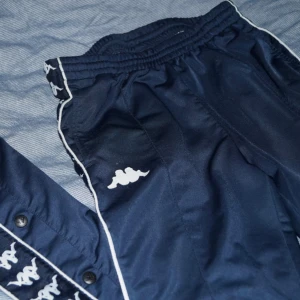  - Mörkblåa träningsbyxor från Kappa med knappar på sidorna. Storlek small. Loggan på framsidan har lossnat i tvätten.