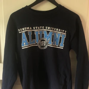 Mörkblå collage tröja - Fin blå collegetröja. Använd fåtal gånger. Passar S/M beroende på hur man vill att den ska sitta. Köpt på second hand. Frakt ingår!