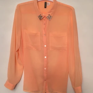  - Skjorta/blusa i fräsch orange färg med strass. Lite transparent material. Från H&M. Helt ny. Oanvänd.