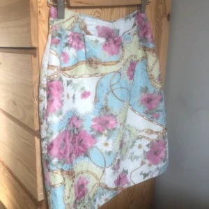 Blommig kjol - Färgglad mönstrad kjol köpt på second hand. Inga synliga defekter förutom att ett litet spänne har lossnat på ena sidan. Lätt att sy fast igen. Ingen storlek men uppskattar denna till en 36:a. Sitter för tajt i midjan på mig som har 38. 