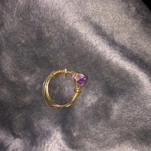 Guldring med lila kristall - Säljer lite ringar som jag gjort själv, ringen är gjord av guldig ståltråd och en lila kristall. Säljer denna ring för 20 kr+ 11 kr i frakt. DMa mig vid intresse!