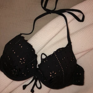 Svart bikiniöverdel - En superfin svart diskret blommig bikiniöverdel från HM. Bikinin knyts runt midjan och i nacken så man kan justera passformen. Knappt använd. Storlek 75B. Köparen står för frakten.