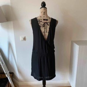  - Cool svart klänning med djup urringning i ryggen. Snygga detaljer i urringningen och band i midjan.