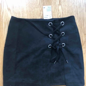  - Kjol med mockaimitation tyg. Knytning framtill och knäppes med dragkedja bak. Upplever den liten i storlek så tror den kan passa även 34 Ny med prislapp kvar!