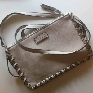  - Frakt ingår! Beige, liten clutch från Don Donna med avtagbar axelrem. Coola detaljer. Perfekt till fest och andra event! 🎀 Sparsamt använd.