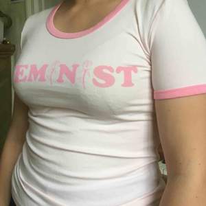 Ljusrosa t-shirt, slim fit. Tryck på bröstet: Feminist. Nyskick. 