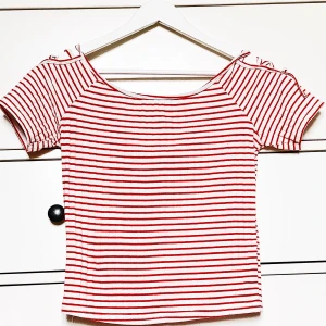 randig topp  - Gullig topp köpt i London. Sparsamt använd i bra kvalitet. Unika rosettdetaljer över axlarna. Rött/vitt randigt är en riktig klassiker! Storleksmässigt passar den en M/L, men även större eller mindre. Fått många komplimanger när jag burit denna topp:) 