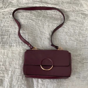 Vinröd väska  - Väska från Anna Field, helt oanvänd, har bara legat i min garderob. Ett medellångt axelband och ett magnetspänne. Väskan är vinröd med guldiga detaljer, superfin!! Möts upp i Stockholm eller fraktar men frakten står du själv för isåfall. 