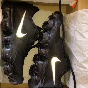 Nike Vapormax svarta  - Säljer dessa helt nya Vapormax från Nike. Helt oanvända samt de är köpt för 1500kr i Nike.se förra året. Snygga som fan samt de har reflex på Nike loggan. Passar till allt och är bekväma, funkar som gym skor också. 