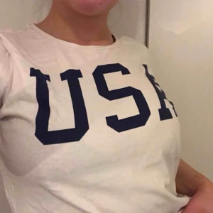  - Vit T-shirt med marin blått tryck USA med ett A på ena armen, super snygg men inte min stil tyvärr🤍 40kr
