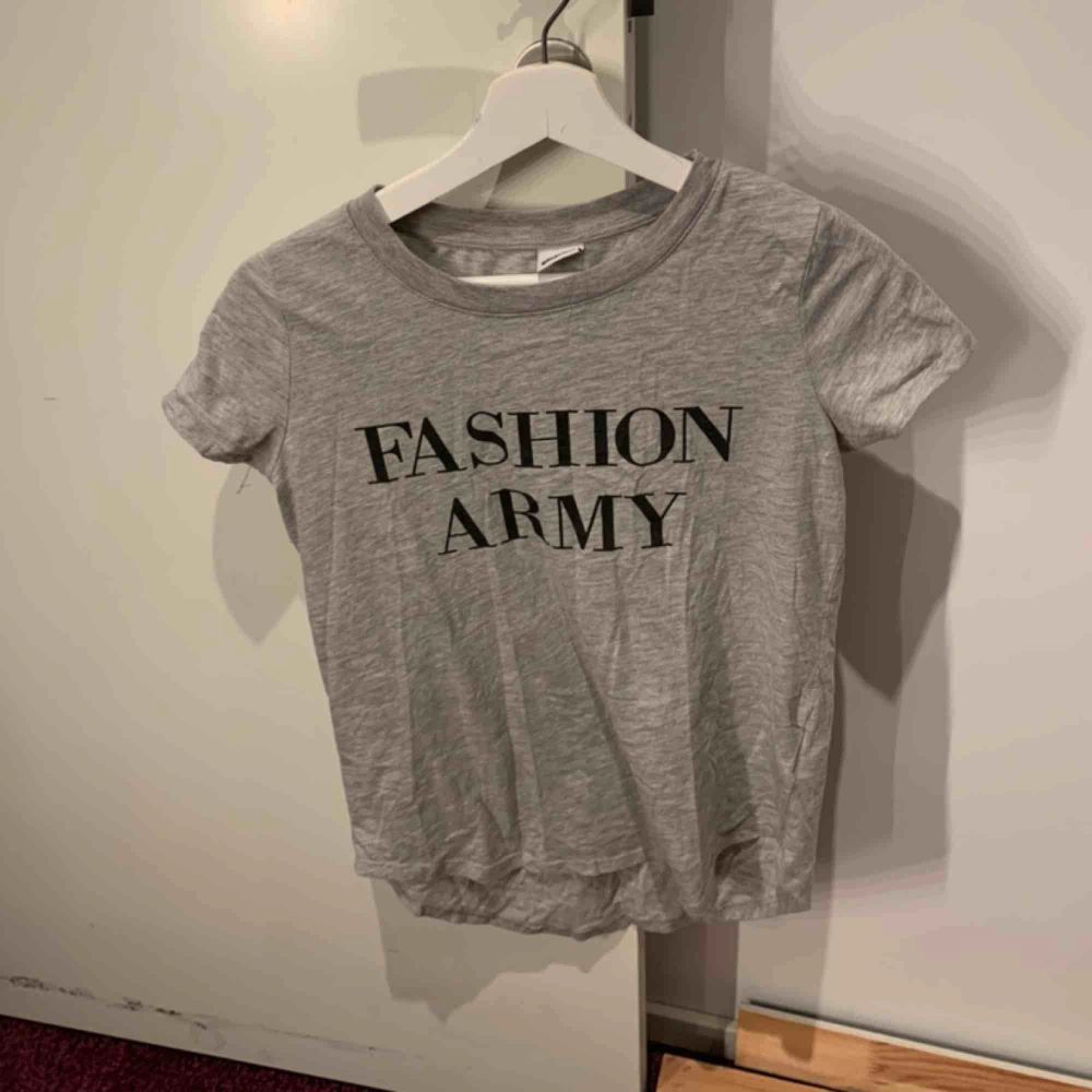 En grå T-shirt med trycket ”Fashion army” från gina tricot. Köpt för något årsedan men enbart använd ett fåtal gånger. Köparen står för frakt . T-shirts.