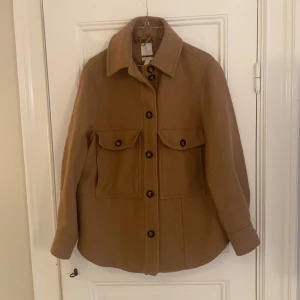 Skjortjacka från h&m - Bomullsjacka från h&m i förra årets modell. Färg: kamel. Jackan har endast används ett fåtal gånger och är i mycket bra skick.  Nypris 799sek