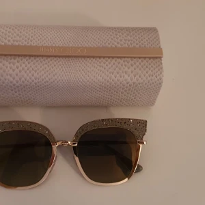 Jimmy Choo Rosy Solglasögon - Har slittåliga bågar av metall. Filtrerar bort reflexer och står emot repor.  Putsduk och fodral ingår. Nyskick, använda endast 2 gånger.