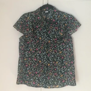  - Tunn blus i svart med blommönster från BikBok i strl S men passar även M. Använd ett fåtal gånger