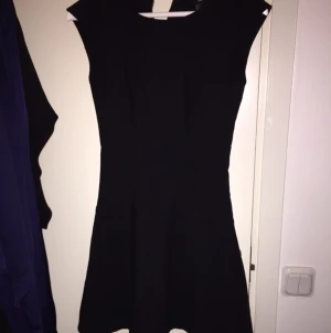  - Svart klänning, 
Den slutar strax över knäna,
Lite volang nertill 
Figursydd.
