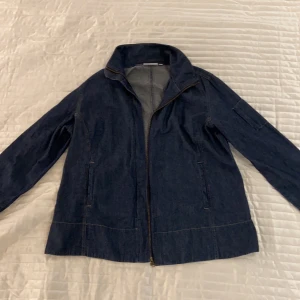 Mörkblå jeansjacka - Mörkblå jeansjacka i strl M/L från Generous. Tunnare jeansmaterial men tjockare tröjor får plats under då jackan är luftig. Dragkedja och framfickor finns.