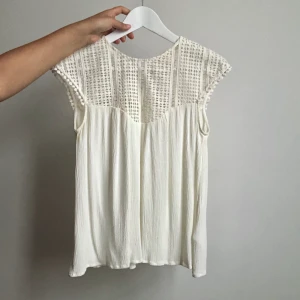 Benvit blus - En superfin benvit blus från H&M i storlek 34/XS. Den har virkad spets över bröstet och axlarna och en knäppning med knapp i nacken. Frakt på 44kr tillkommer om den ska skickas.