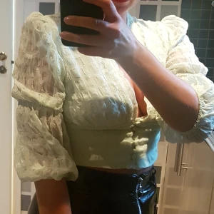 Ljusgrön topp med puffärm  - Ljusgrön topp i fint material med en liten puffärm. Toppen är kroppar med ljus urringning och knappar.