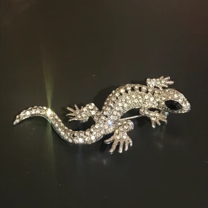 Ödla brosch - En fin brosch som ej har gått till användo. 7 cm i längd. Fina glittrande stenar, ingen har lossnat. Frakt är 11 kr 🥰