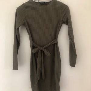 Klänning med knytband - Långärmad klänning i en militärgrön färg från boohoo. Har ett fint knytband som man knyter i midjan som framhäver ens former. Strl 36. Aldrig använt endast testad. 