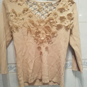  - Vacker topp i beige ton med nät på ryggdelen och blommor både fram och bak.  Toppen är stretching vilket innebär att den även kan passa en L.  Den är lite skrynklig på bilden men det är för att jag har haft den intryckt i en låda. Låt den hänga eller stryk den lite så blir den slät igen! 