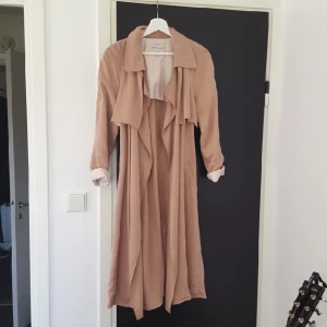  - Trenchcoat i fin gammelrosa färg. Bilderna gör inte färgen helt rättvisa! Helt oanvänd, men med ett skönhetsfel som ni kan se på andra bilden, går säkerligen att tvätta bort. Köptes för 600kr (kostade egentligen 800 men fick reducerat pris pga den svarta lilla fläcken). Kan fraktas för en 50 lapp extra🌼 