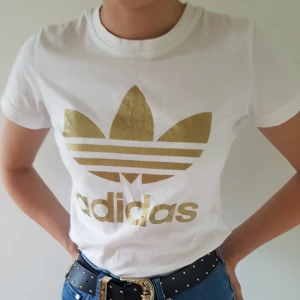  - En vit adidas t-shist med guldfärgad logga på framsidan. Är storlek 36 men skulle säga att den passar bättre på en 34 då den är liten i modellen. Använd endast 1 gång då det inte är min stil. Köparen står för frakten!🌻