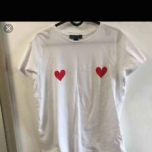Vit T-shirt med två röda hjärtan som tryck. Tröjan är från primark och är i storlek XS/S. Använd 1-2 gånger, en gång ute och en gång hemma så skicket är som nytt. Helt felfri!