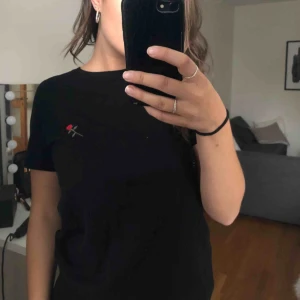  - En svart t-shirt med en broderad ros på bröstet, från NAKD. Köparen står för ev frakt😊