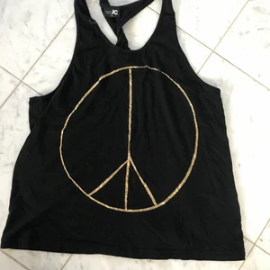 Flowigt linne - Svart linne med guldigt peace märke. Banden är snurrade i ryggen. Gott skick. Storleken är XS, men passar säkert även större storlekar. 