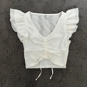 Vit topp - Vit topp med korta volangärmar och v-ringning. Toppen har en fin knytning framtill, är dekorerad med spetsdetaljer och har en dragkedja i sidan.. Perfekt sommar topp!💗🫶🏼