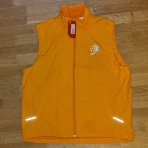 Orange väst från Puma - Orange väst från Puma, helt ny och oanvänd. Den har reflexdetaljer och insidan är av mjuk fleece.