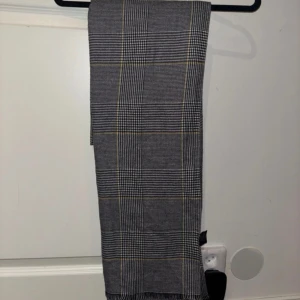 Rutig halsduk från Lindex - Snygg rutig halsduk från Lindex i grått med inslag av gult. Perfekt för att hålla dig varm under kyliga dagar. Den har en klassisk design som passar till många olika outfits.