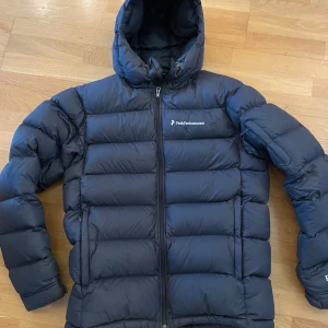 Mörkblå dunjacka från Peak Performance - Hej! Säljer denna peak performance jackan. Den är andvänd men fortfarande i väldigt fint skick. Den har 2 fickor vid magen som vanligt men och 2 på innersidan och en på armen. Den är väldigt varm och perfekt för kalla vinterdagar. Nypris 4000kr