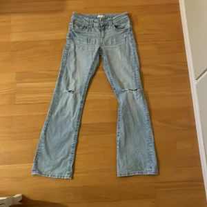 Ljusblå jeans med slitningar - Säljer ett par ljusblå jeans från Gina med slitningar vid knäna. De har en klassisk femficksdesign och är i en straight passform. Säljer då de inte sitter bra på mig