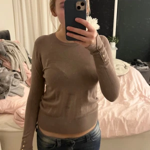 Beige ribbad tröja med knappar - Säljer en stilren beige ribbad tröja med långa ärmar och dekorativa knappar vid ärmsluten. Passar bra till jeans eller kjol. Skriv om ni har några frågor!💞