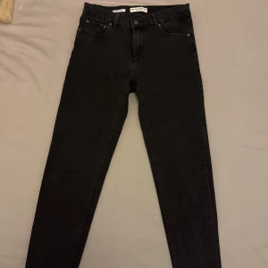 Svarta jeansbyxor - Snygga svarta jeansbyxor med en klassisk design och stretch. De har en knapp och dragkedja framtill samt fem fickor. Perfekta för en stilren look. Det finns fläckar och har inte testat att ta bort fläckarna. Se bild.