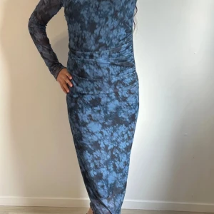 Blå mönstrad långklänning - Snygg blå långklänning med ett unikt mönster. Klänningen har långa ärmar och en tight passform som framhäver figuren. Perfekt för en stilfull look. Köpete för 500kr