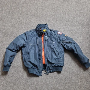 Svart bomberjacka från Parajumpers - Snygg svart bomberjacka från Parajumpers med orange foder. Jackan har flera fickor, dragkedja och en broderad patch på ärmen. Perfekt för höst och vår.kvitto finns 4500 jag köpte på NK