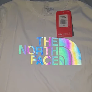 Vit t-shirt från The North Face - Säljer en vit t-shirt från The North Face med ett coolt holografiskt logotryck på framsidan. T-shirten är kortärmad och har en klassisk passform. Storlek M och helt oanvänd. Vid frågor är det bara att skriva😀