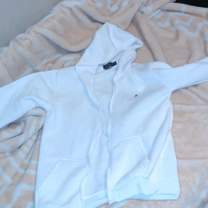 Vit hoodie från Ralph Lauren - Säljer en stilren vit hoodie från Ralph Lauren med dragkedja och huva. Den har en liten broderad logga på bröstet och två praktiska fickor framtill. Perfekt för en avslappnad look. Inte en riktigt ralph lauren 