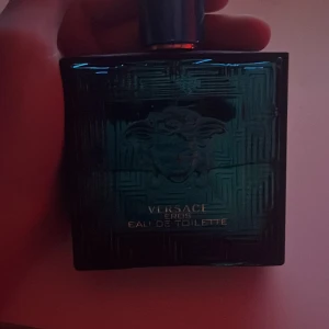 Versace Eros Eau de Toilette - Säljer en elegant Versace Eros Eau de Toilette i en stilren blå glasflaska med det ikoniska Medusa-huvudet. Perfekt för den som vill ha en doft med karaktär och stil. Flaskan har en fyrkantig form och en praktisk sprayfunktion.
