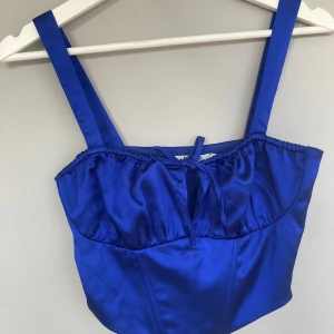 Blå korsettopp från NA-KD - Snygg blå korsettopp från NA-KD i satin med smala axelband och knytning framtill. Perfekt för nyår🥰
