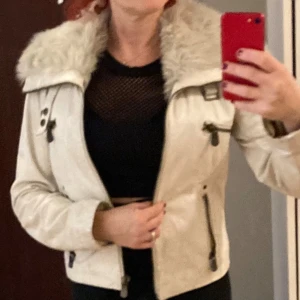 Beige jacka med pälsdetaljer från Rock'n Blue stl 36 - Snygg beige jacka från Rock'n Blue med pälsdetaljer på kragen. Jackan har dragkedja och knappar framtill samt två fickor med dragkedja. Perfekt för kyligare dagar.superskön på. Har använt den endast ett par gånger. Mkt fint skick