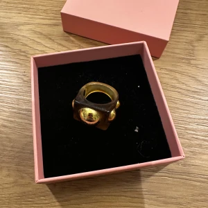 Guldfärgad ring med stora detaljer - Säljer en unik guldfärgad ring med stora, iögonfallande detaljer. Från lizmo, har en liten repa på stenen i mitten