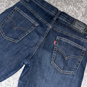 Levi's jeans i mörkblå denim - Snygga Levi's jeans i mörkblå denim med klassisk femficksdesign och kontrastsömmar. De har en rak passform och är perfekta för en avslappnad stil. Levi's logotyp syns på bakfickan och knappen framtill.