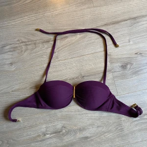 Lila bikiniöverdel med knytband - Snygg lila bikiniöverdel med knytband i nacken och ryggen. Den har en stilren design med gulddetaljer på banden. Perfekt för en dag på stranden eller vid poolen.